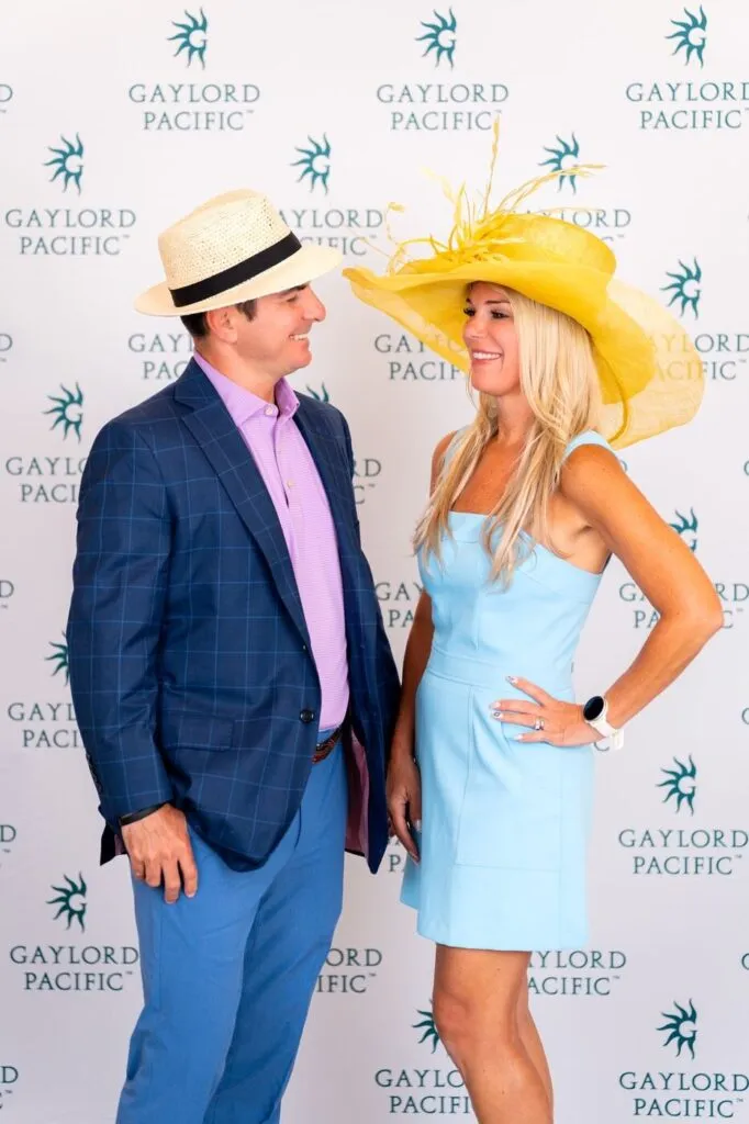 A couple in race-day hats posing at the Gaylord Pacific step-and-repeat at the Del Mar racetrack