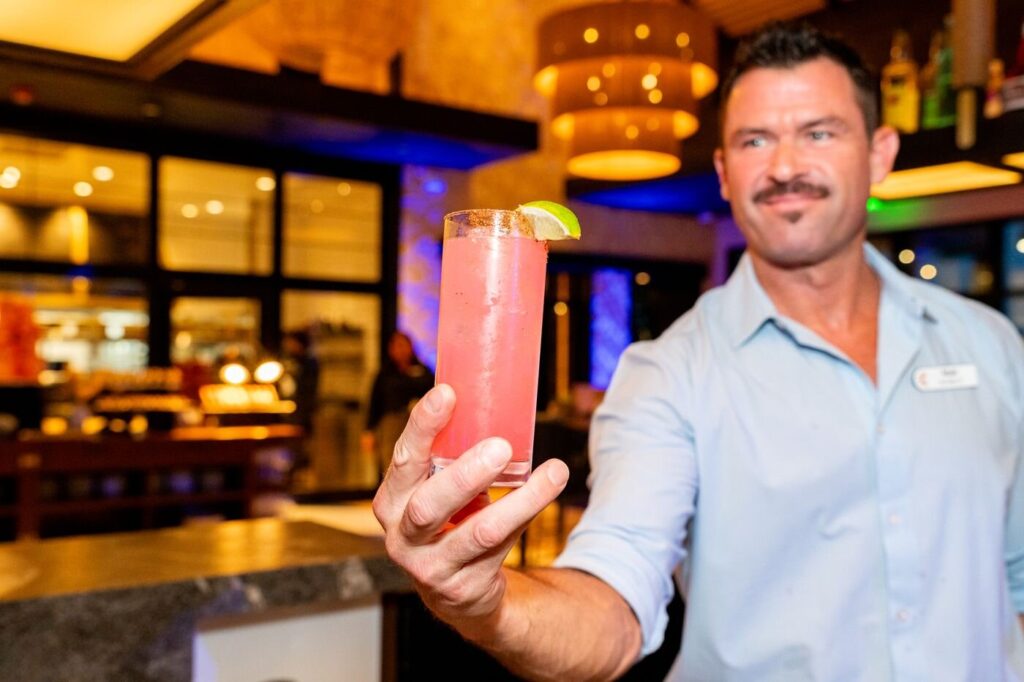 A bartender raising a pink cocktail toward the camera at the Marzul bar