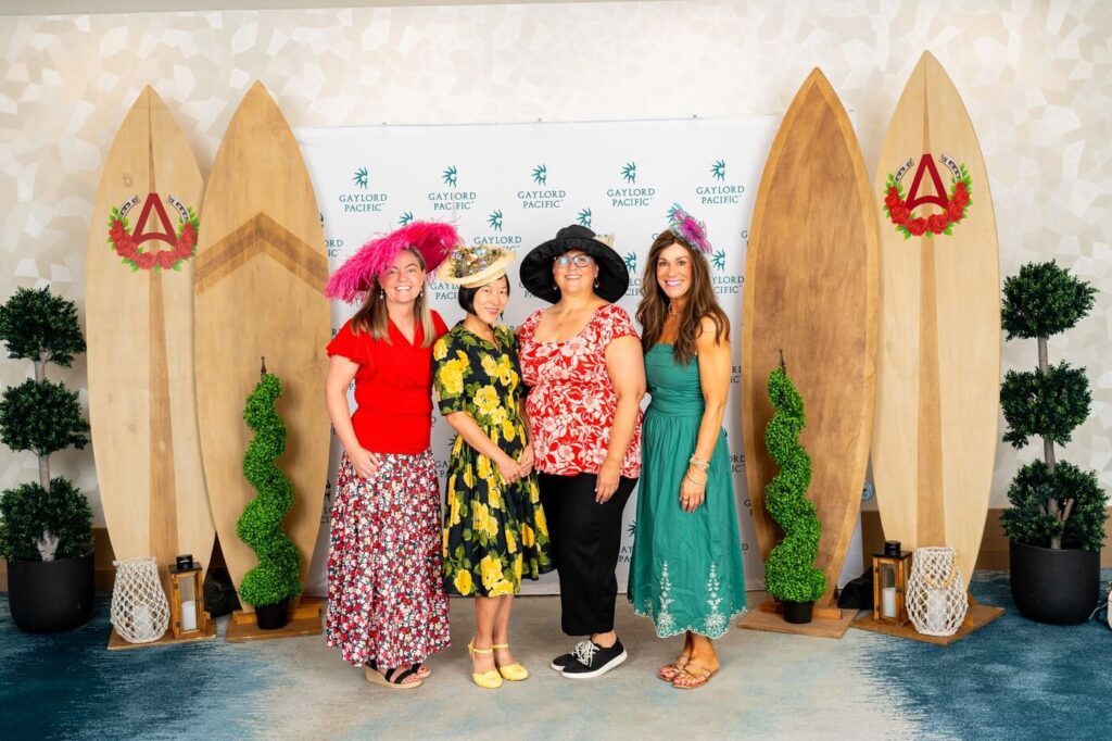 A group of guests in derby hats posing together at the Gaylord Pacific racetrack event
