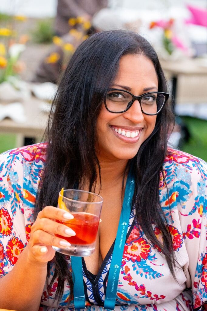 A guest in a floral top smiling over her cocktail at the Marzul grand opening