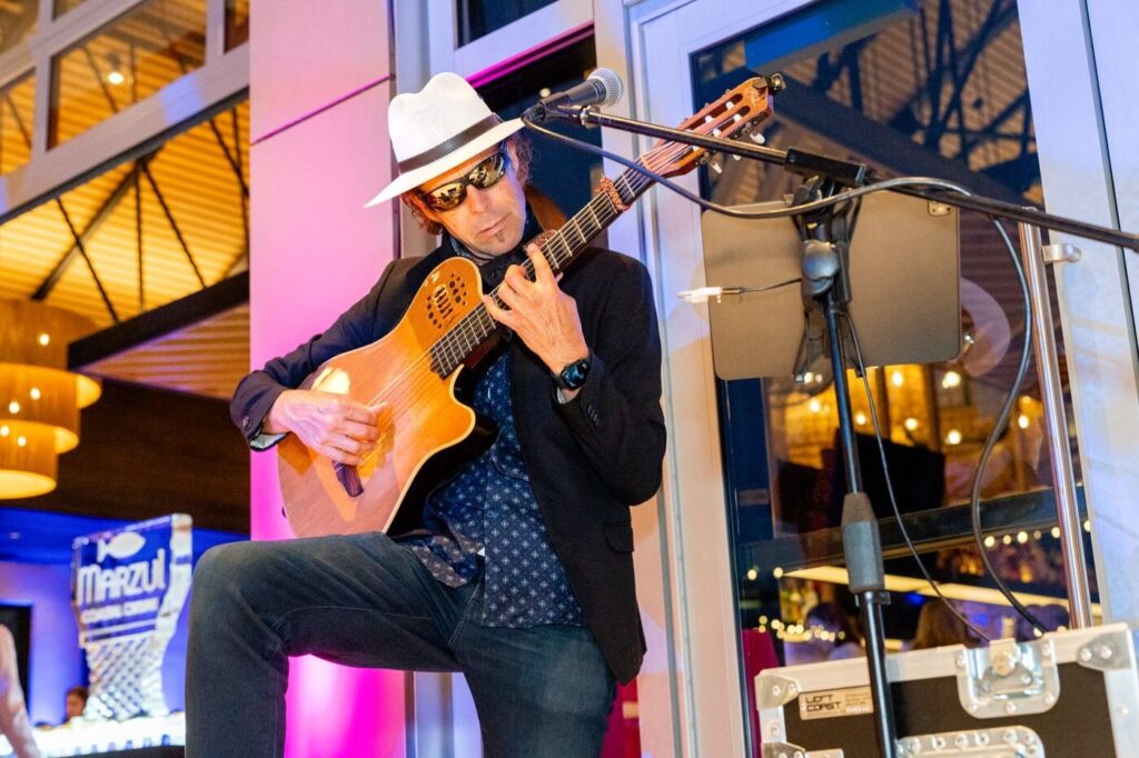 A guitarist in a white hat playing under pink light at the Marzul grand opening