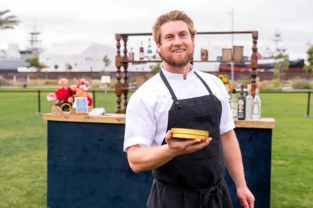 A chef in a black apron smiling with a plate at the Marzul grand opening