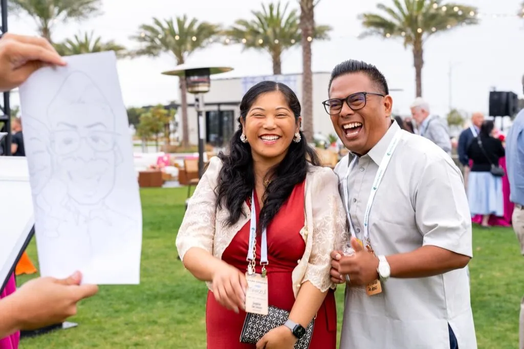 Two guests laughing at a caricature of themselves at the Marzul grand opening