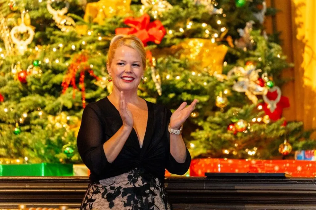 The host clapping in front of the Christmas tree at a company holiday party