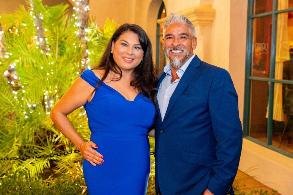 A couple in blue posing among the lights at a company holiday party at the Prado