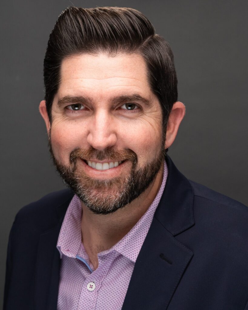 Corporate headshot of a bearded man in a navy blazer, shot at his company office