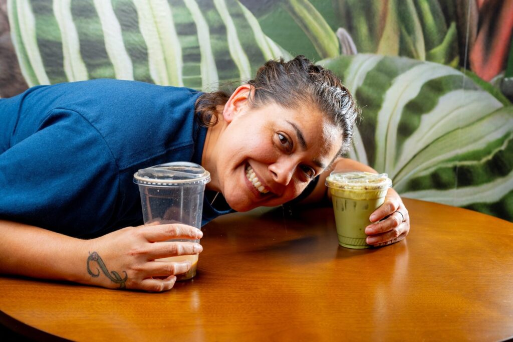 A cafe team member grinning beside a fresh juice, product shot with a person