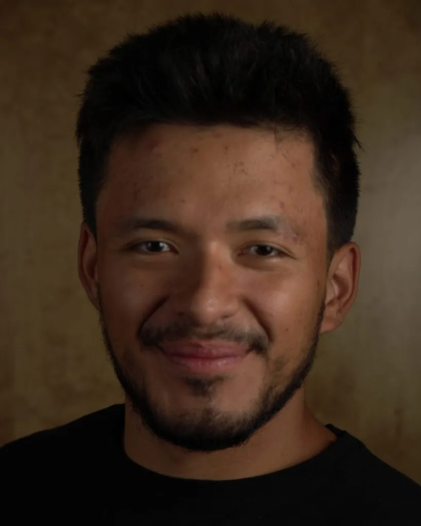 Headshot of a smiling young man in a black tee on a warm brown backdrop