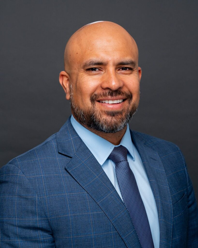 Law firm headshot of a smiling man in a blue plaid suit