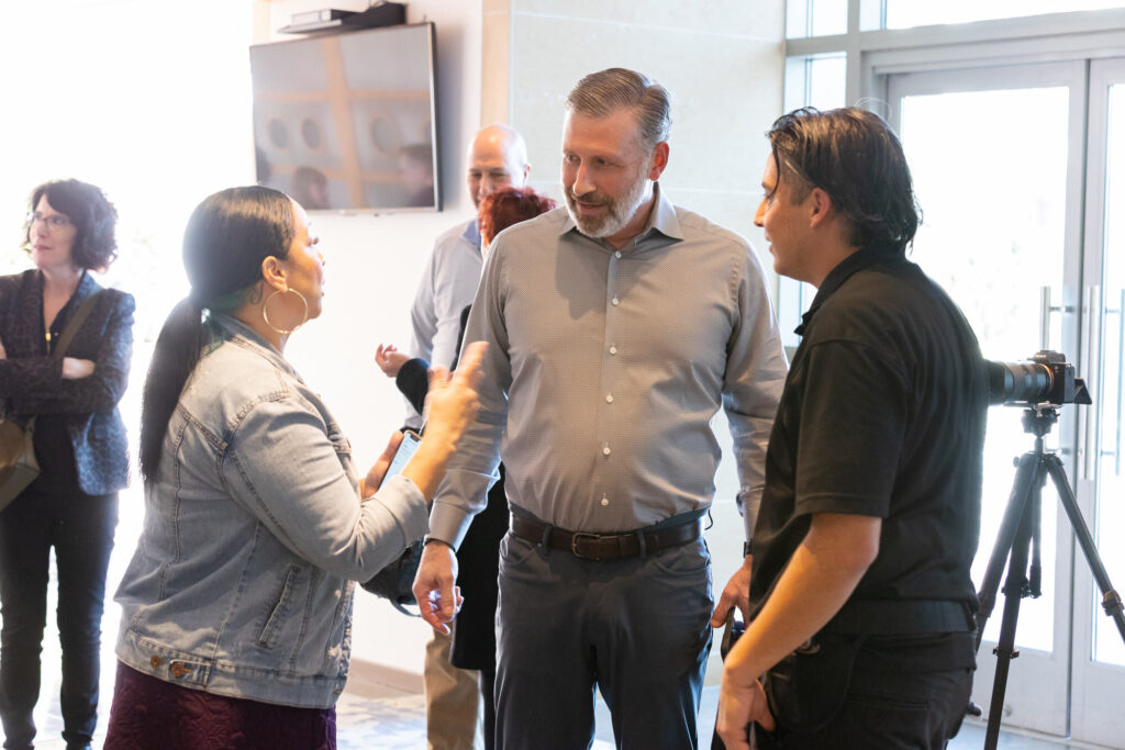 Eddie Flores talking with an FMG Leading leader and a team member between shots, his camera on a tripod beside them
