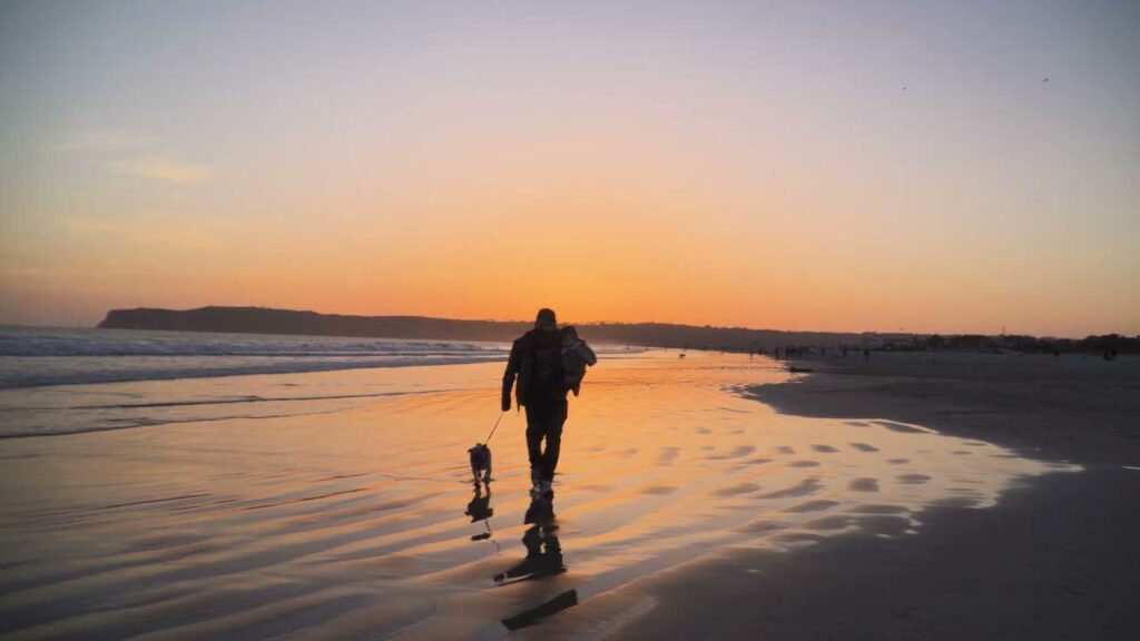 Eddie walking his family home along the beach at sunset, in silhouette