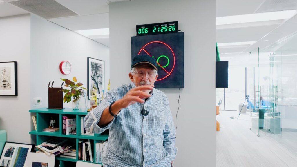 A speaker in a cap talking with his hands in a bright office, from an Ask Turing short