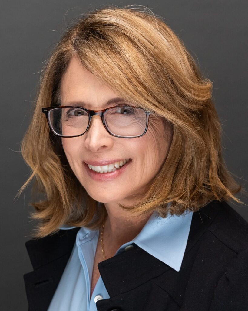 Corporate headshot of a woman with glasses in a black blazer and light blue collar