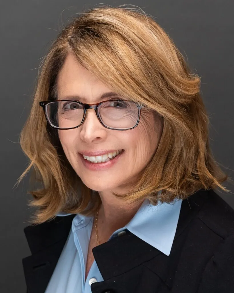 Corporate headshot of a woman with glasses in a black blazer and light blue collar