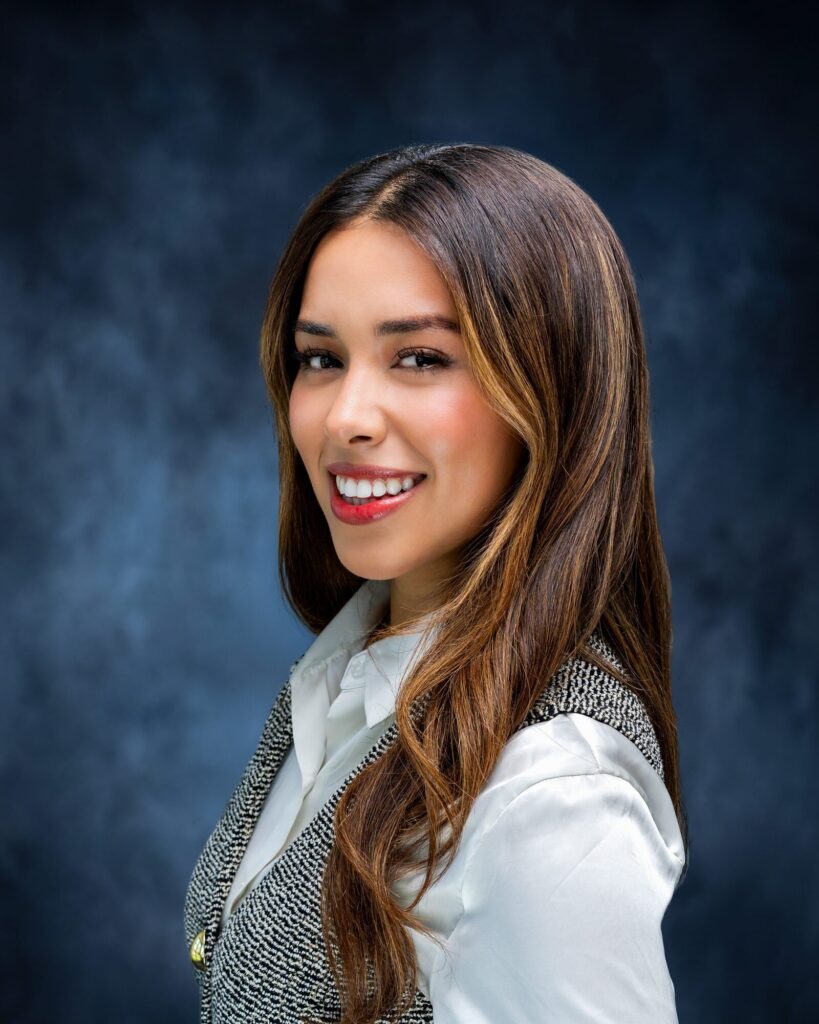 Team headshot of a smiling woman on a painted blue backdrop