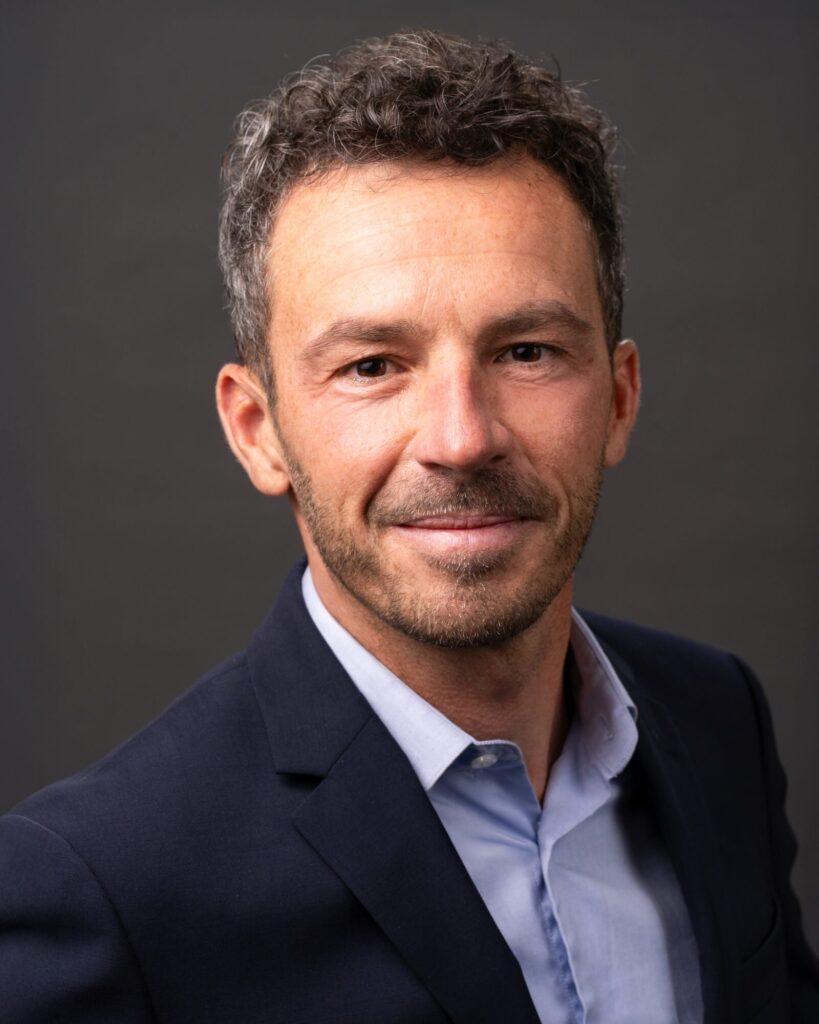 Professional headshot of a man in a navy blazer and open collar
