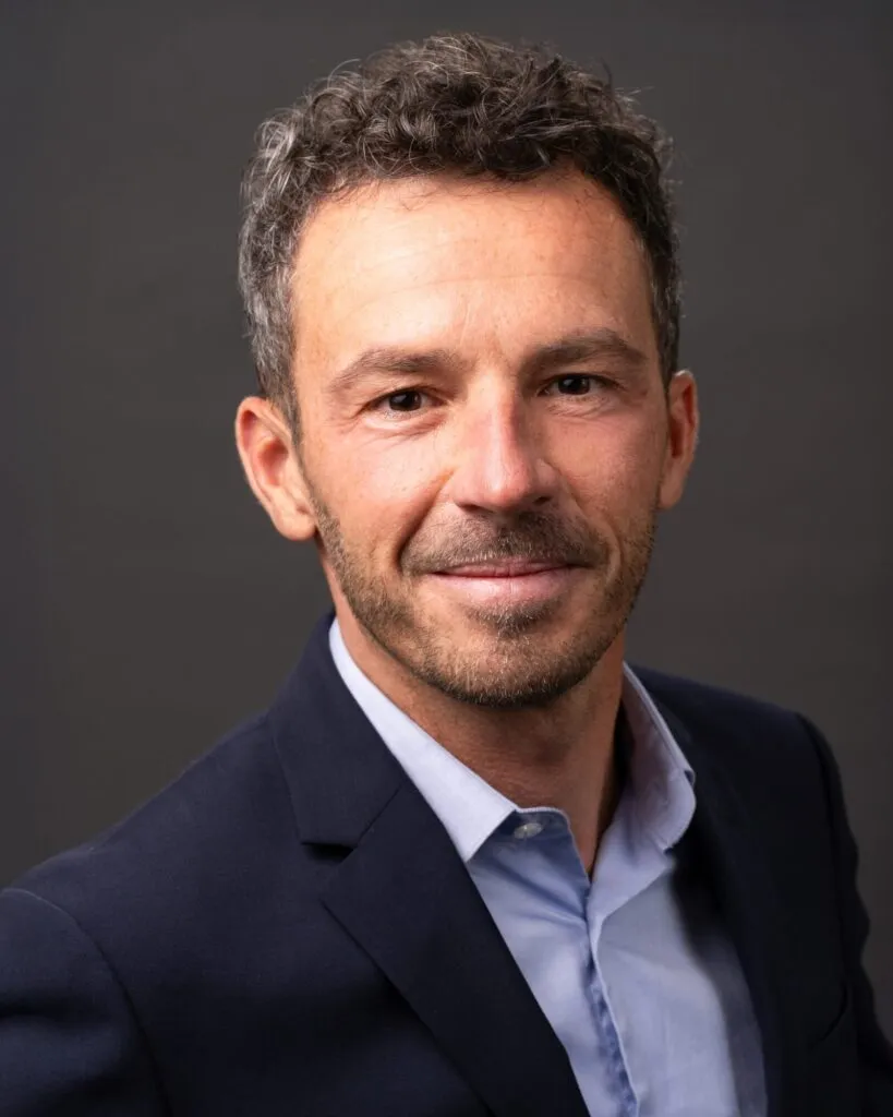 Professional headshot of a man in a navy blazer and open collar
