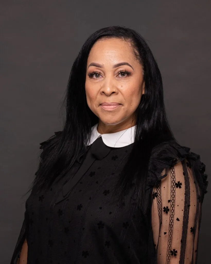 Business headshot of a smiling woman in a black blouse against a dark backdrop