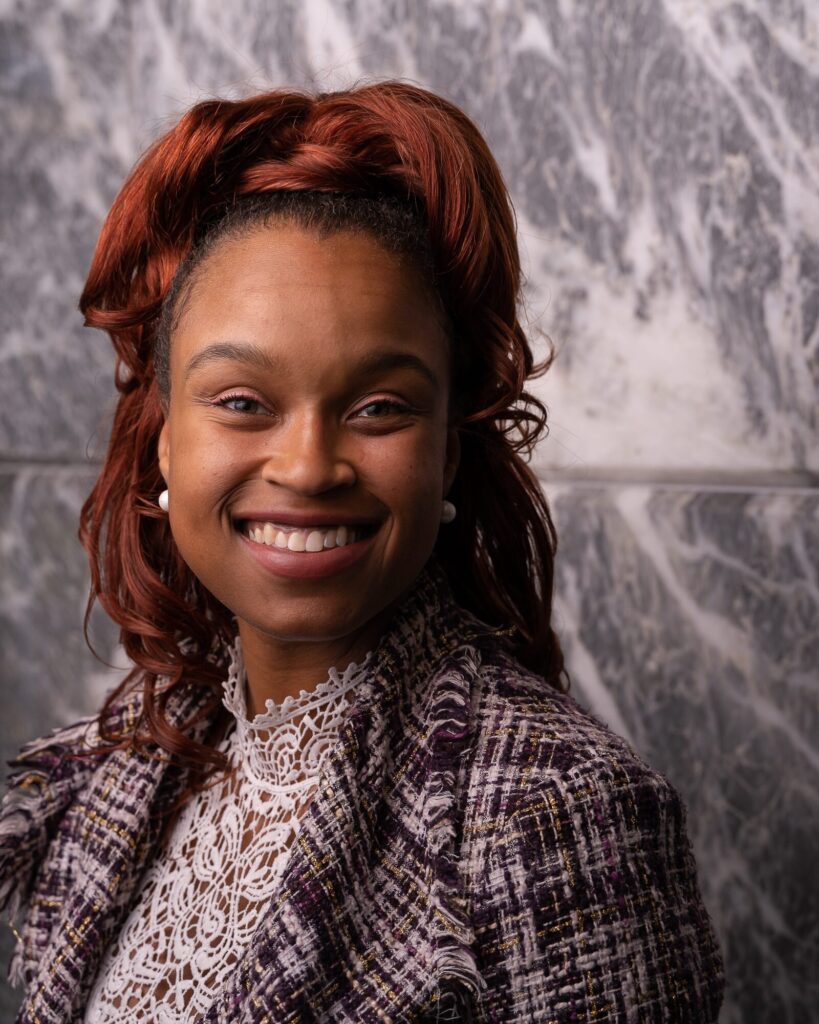 Business headshot of a smiling woman in a tweed jacket against a marble wall