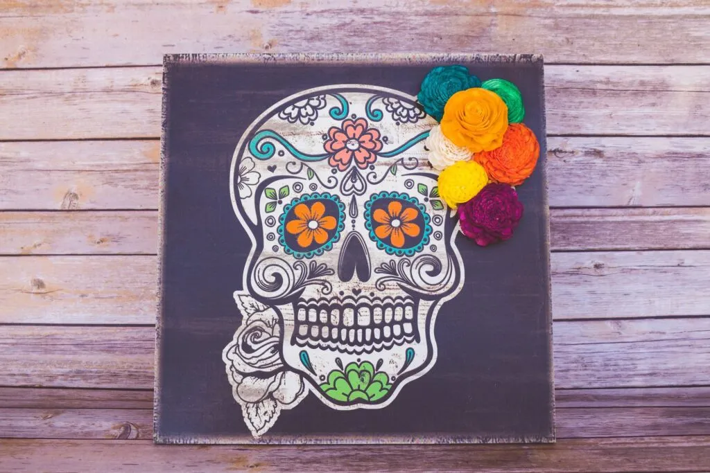 Painted sugar skull sign with paper flowers on a wood backdrop