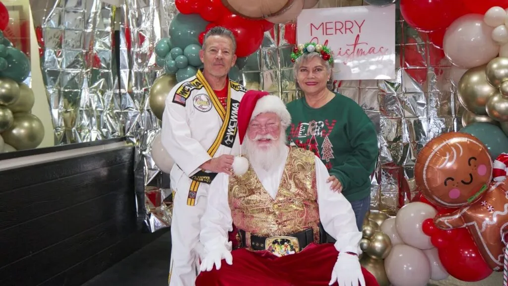 The West Coast Martial Arts instructor in his gi standing beside Santa and a guest in front of holiday balloons